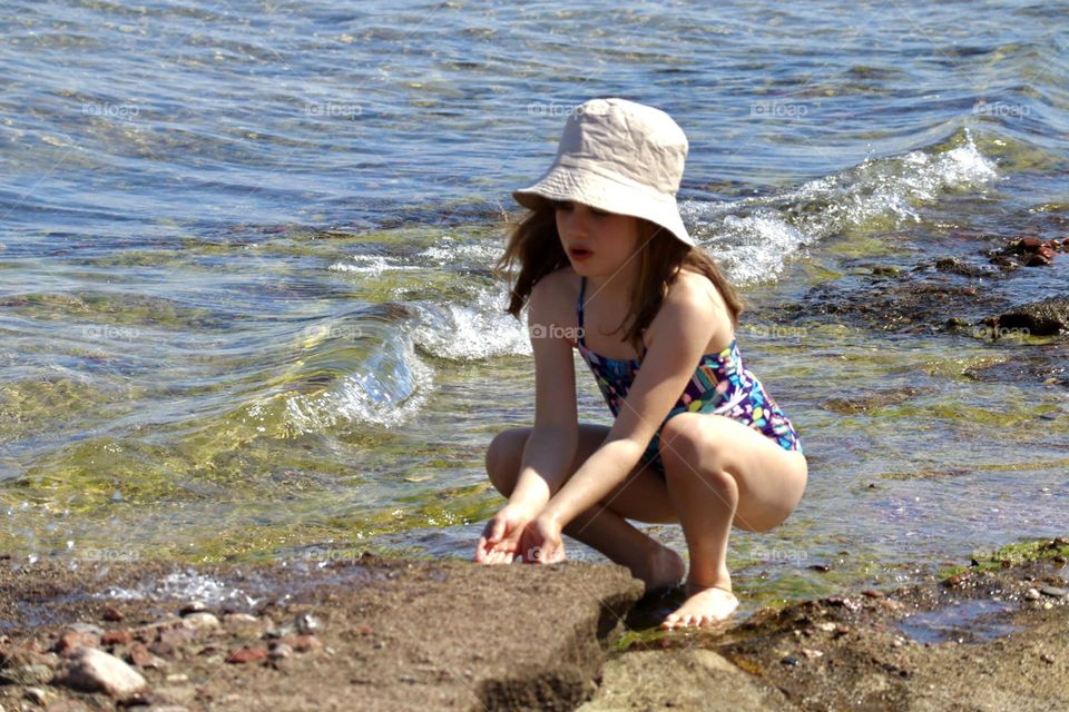 A girl with hat sitting by the water