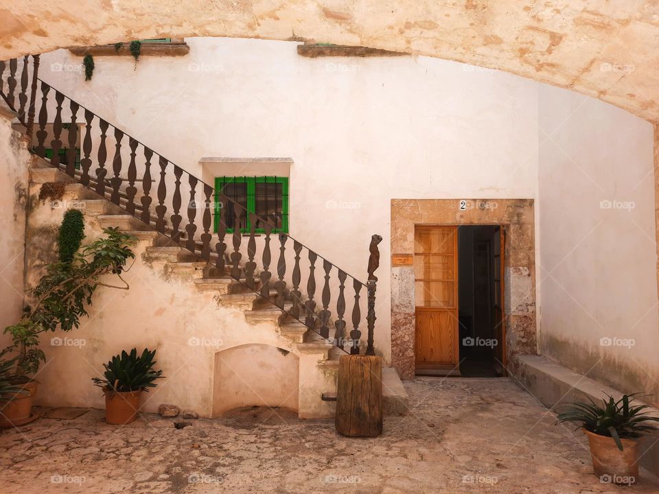 Mediterranean traditional courtyard at a rural old manor. Facade with white wall, wooden door and green Majorcan blinds. Stairs with cast iron stair rail. Calvia, Majorca, Spain.
