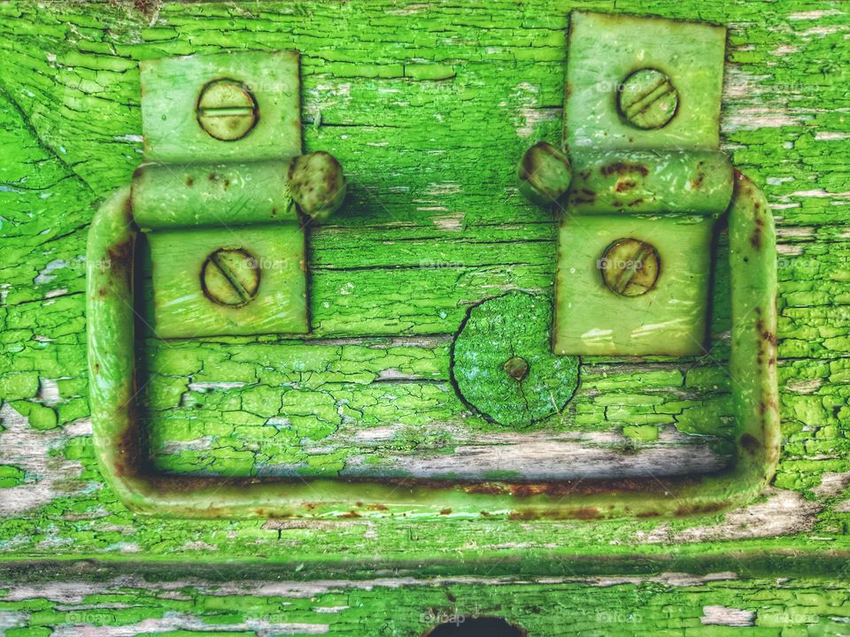 a bright green wooden box with a metal handle fastened with screws using two rectangular metal hinges. peeling old green paint.