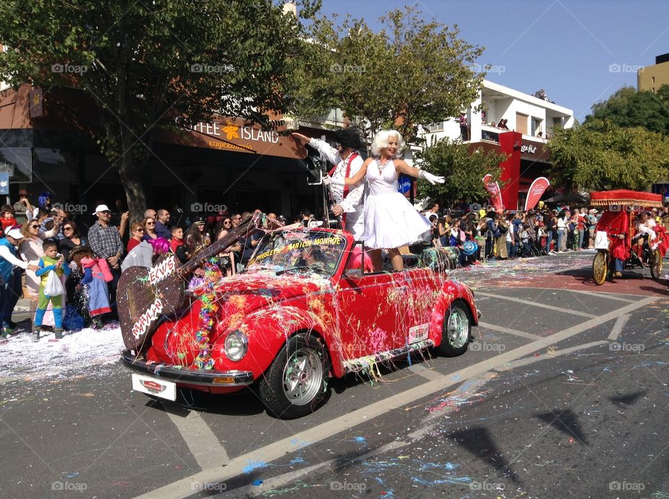 Elvis Presley and Marilyn Monroe riding on a red VW convertible in carnival parade.