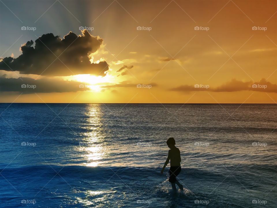 Wonderful golden sunset rewards a small boy in the ocean.
