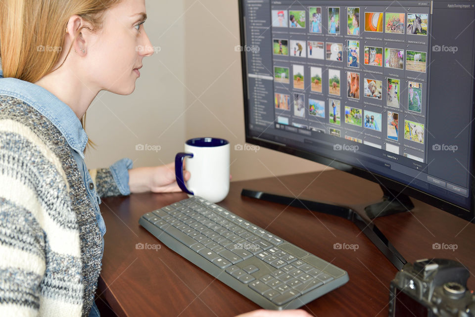 Woman sitting at a desk while drinking coffee and editing pictures on a computer