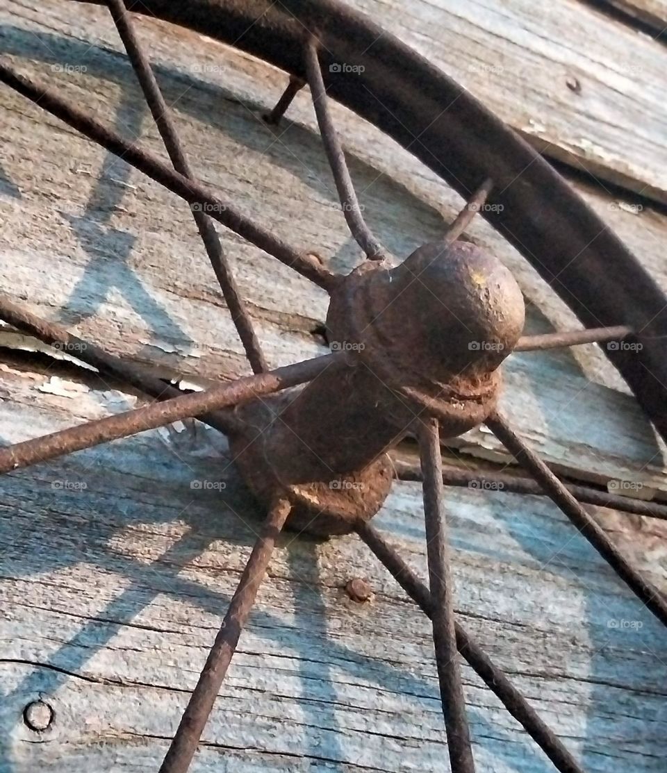 An Old Rusty tricycle wheel hanging on a wood panel wall .