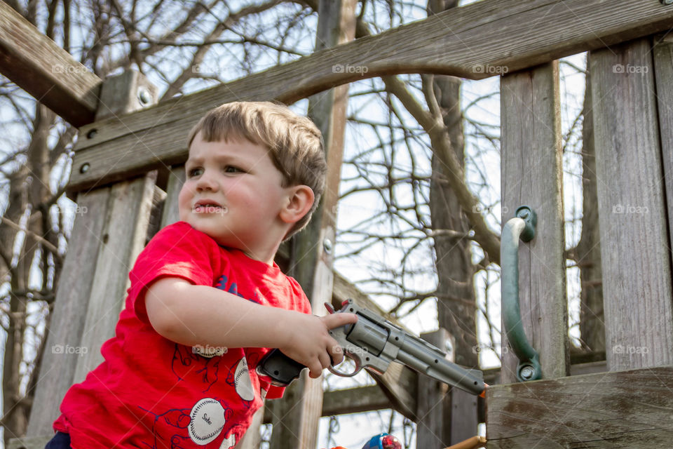 Cute kid with gun near wooden gate at outdoors