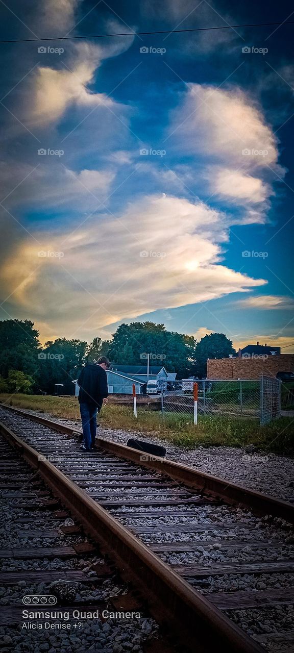 A wonderful background of a sunset puffy cloud filled sky in a small town of a boy walking down the tracks