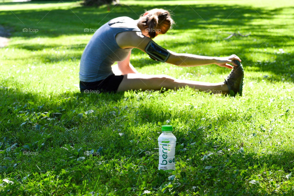 Bottle of Berri fit in the grass and a woman in the background stretching