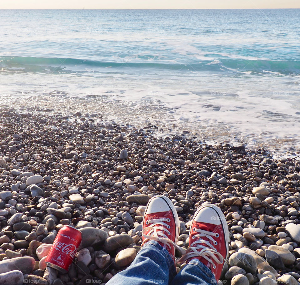 A can of Coca Cola on the beach with red sneakers.