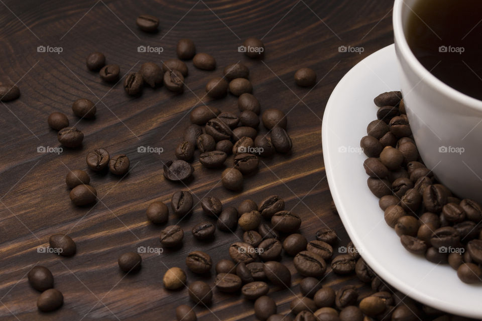 cup of coffee on a dark wood table,  coffee beans as background.  beginning of daily morning concept!