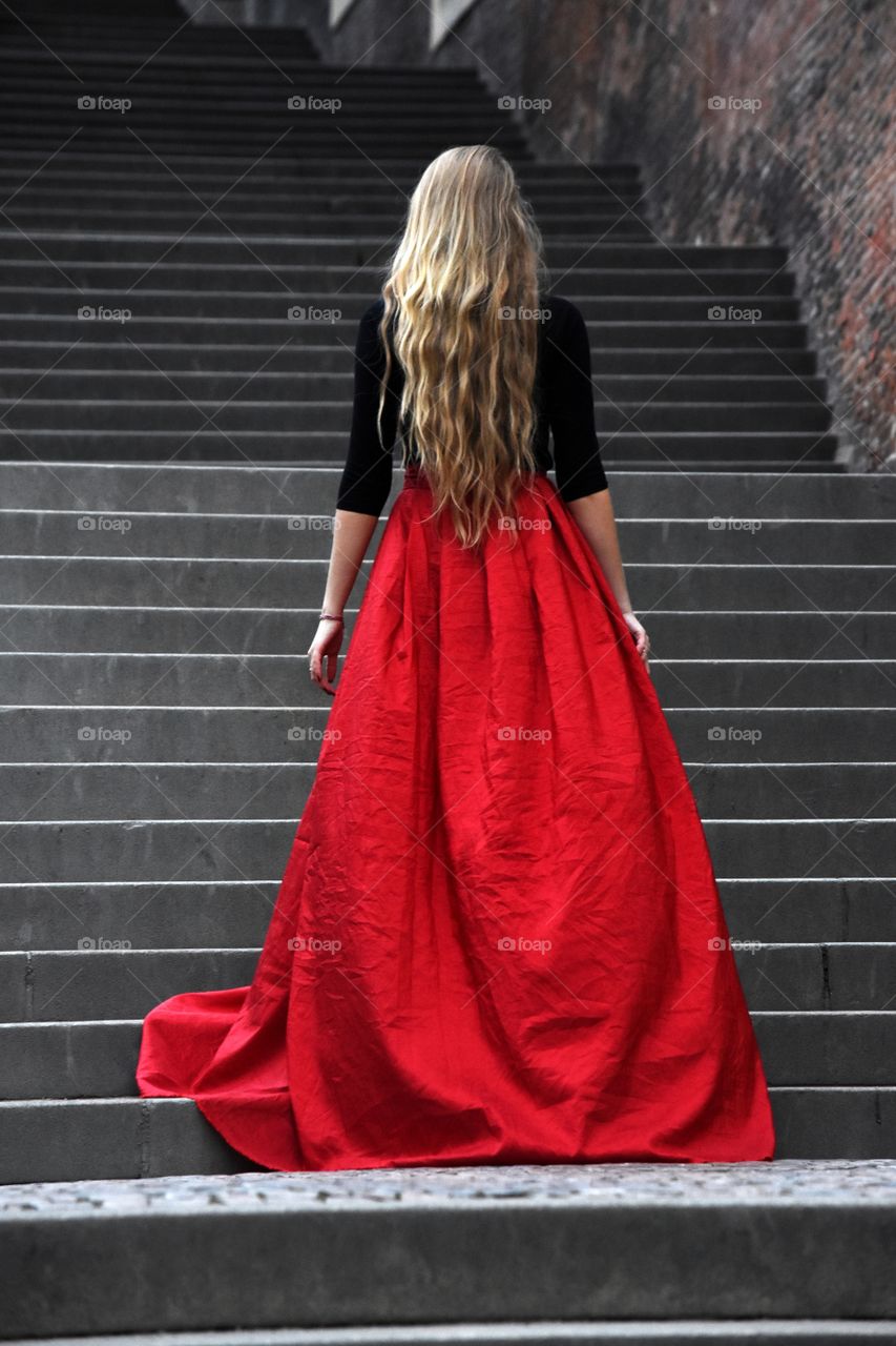 Blonde long hair woman in long red skirt standing on the stairs in old Prague
