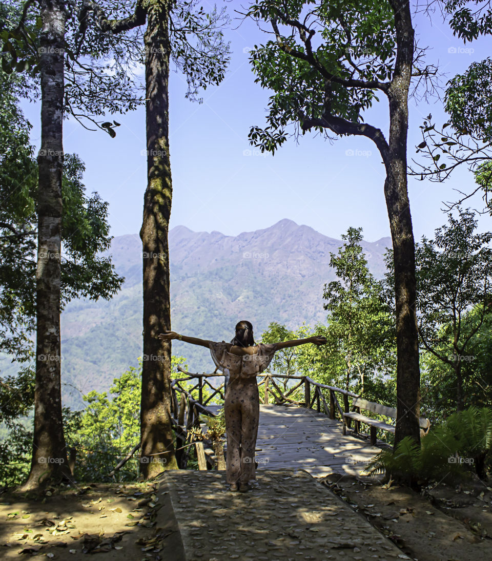 Women raise their arms Background trees and mountains at Nern Chang Puak View Point , Kanchanaburi, Thailand.