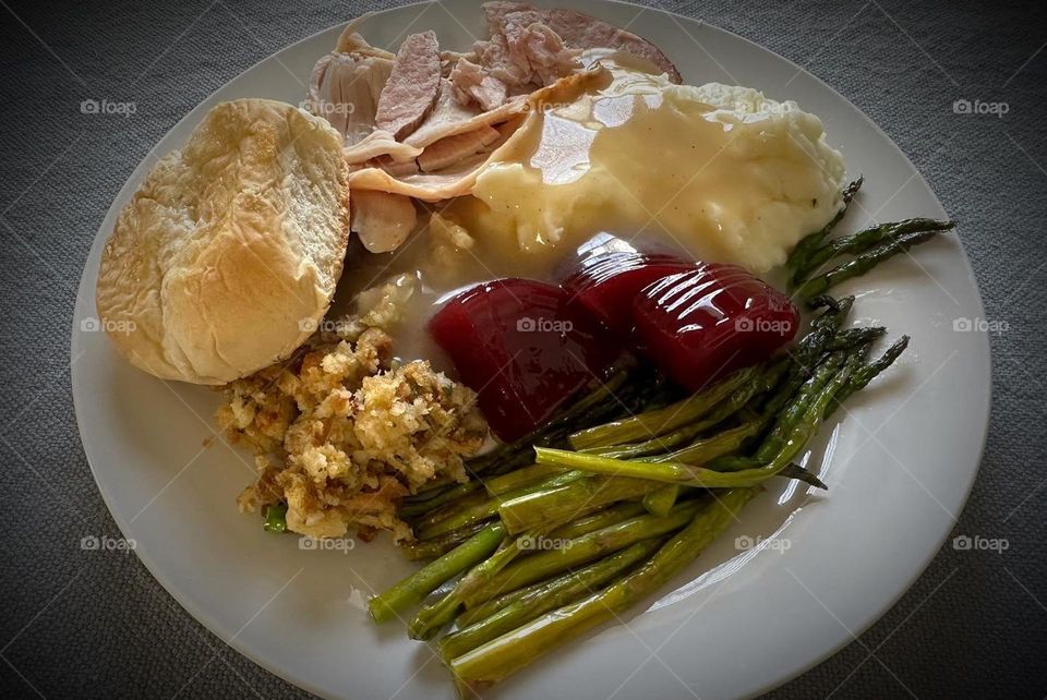 A Thanksgiving meal with ocean spray cranberry sauce, asparagus, mashed potatoes, turkey, stuffing, dinner roll and gravy.