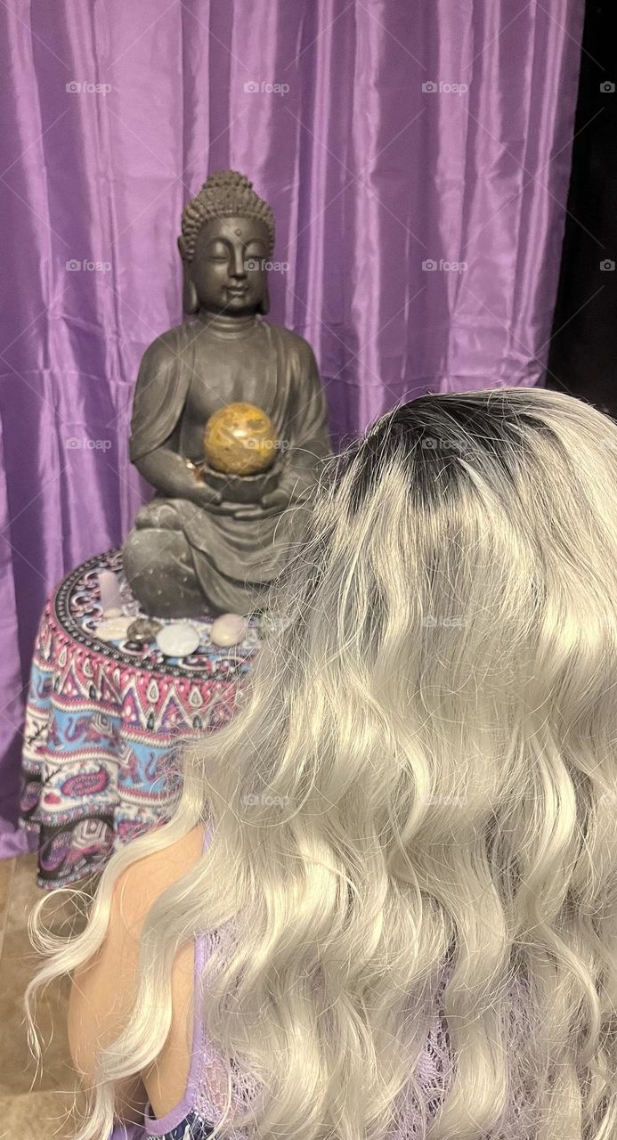 A woman meditating with a Buddha statue on a stand.