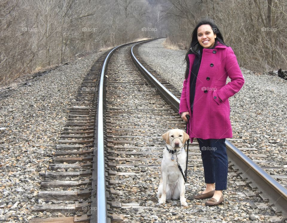 Spring walk with your dog, girl wearing a fuchsia jacket standing with her yellow lab on railroad tracks 