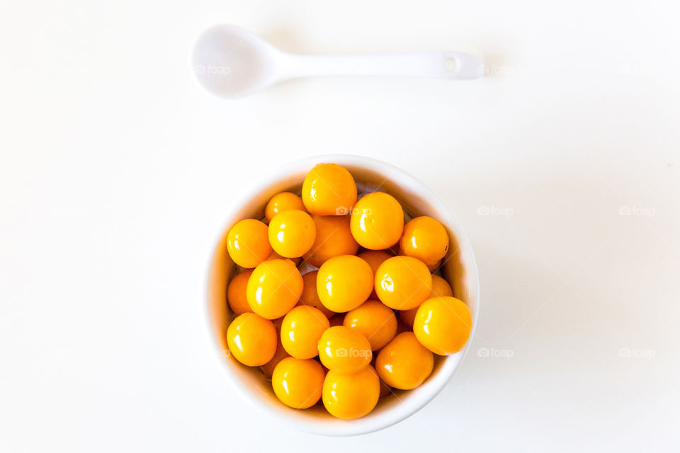 Simple minimalist composition of white bowl filled with fresh gooseberries with a white spoon. White background lay flat. Healthy fresh summer fruit in a bowl for a healthy lifestyle.