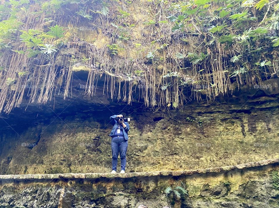 A photographer standing on a walkway next to a cenote 