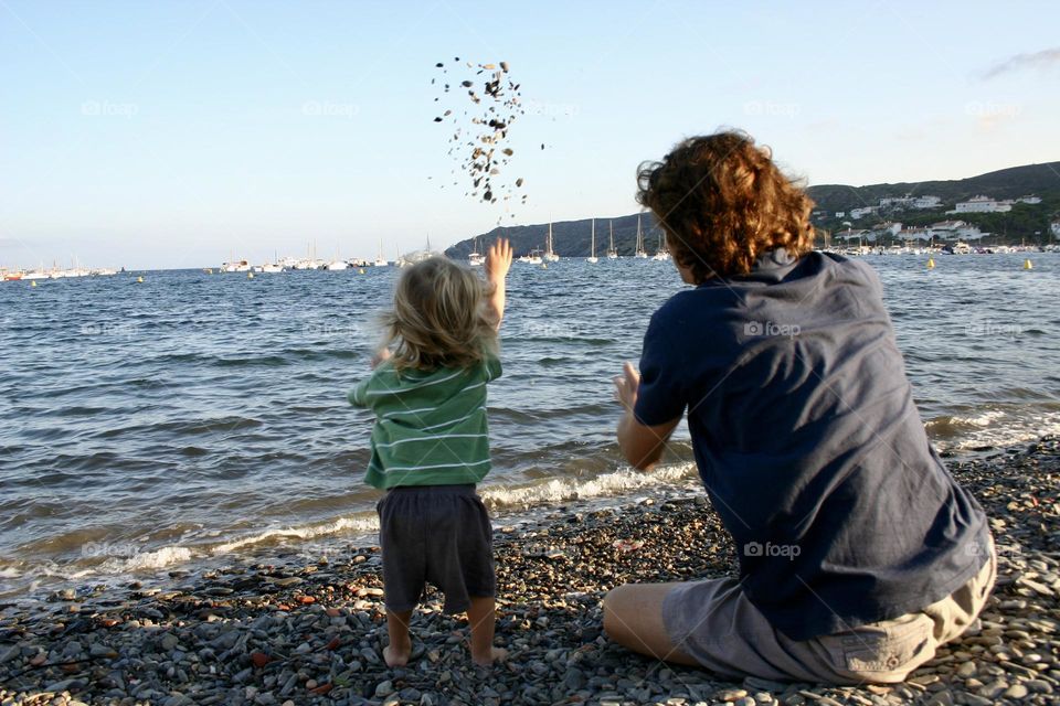 Little kid throwing little stones into the sea