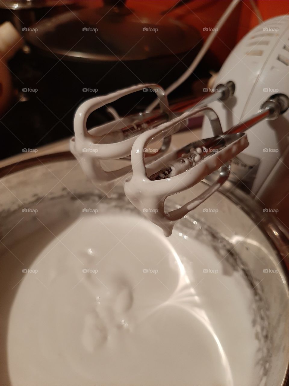 One of the daily activities is preparing sweets for tea. Photo white cream dripping from the beaters of the mixer in a metal Cup with cream.