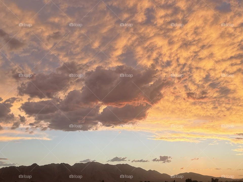A bright orange sunset with the blue sky and mountains below it.