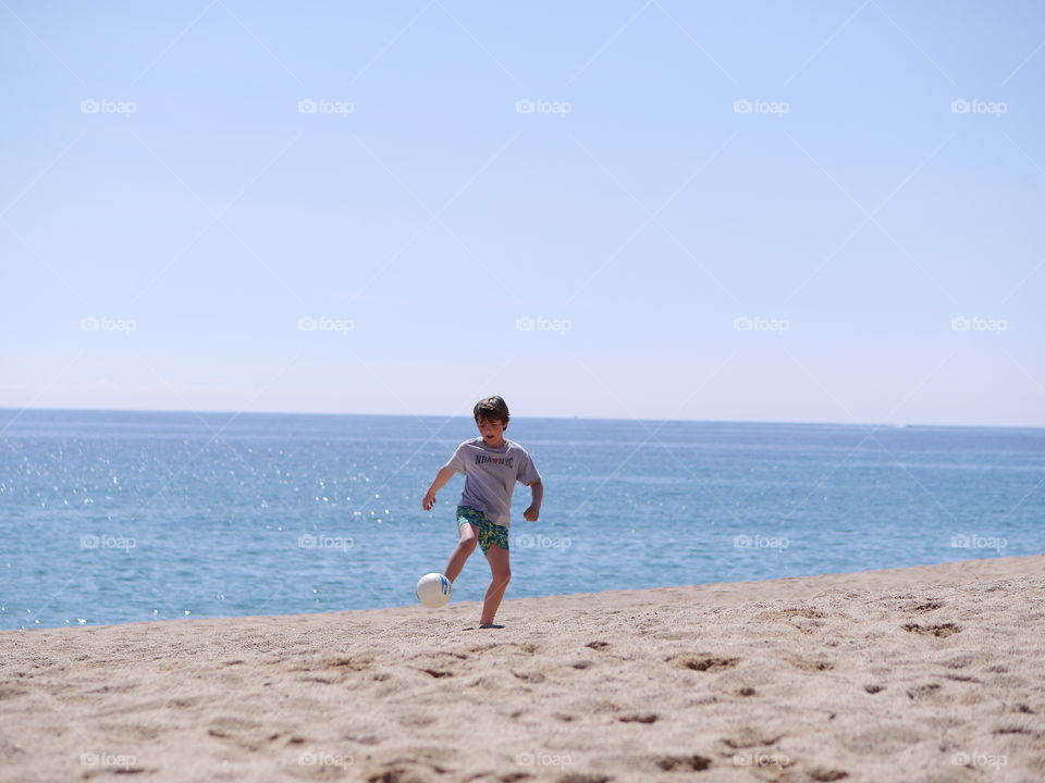 Boy playing with football at beach