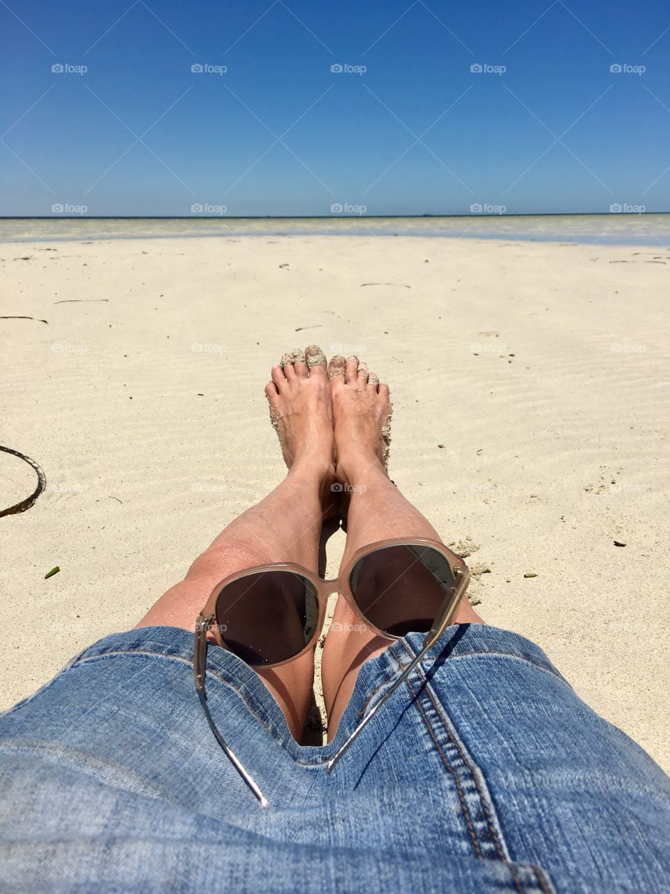 Remote pristine beach, lower body, leg shot woman sitting toward ocean horizon on sand 