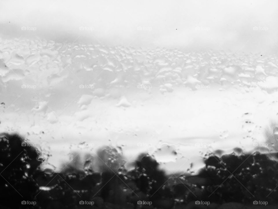 A rain smeared window blurring the countryside side view, overlooking the tree tops looking for the brighter skies to come. 