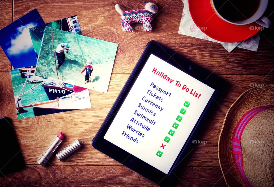 A desk top flat lay with a holiday to do list showing on a tablet and vacation photos too.