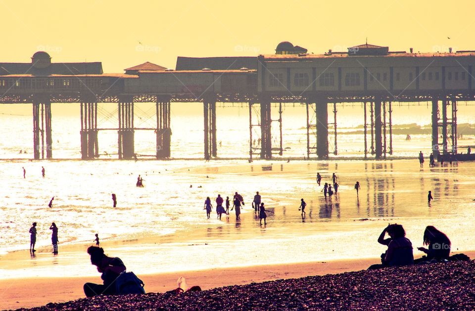 Hazy sunshine on a hot summer’s day, silhouettes the people on the beach and the pier stretching out into the sea - Hastings, East Sussex, UK - 2008