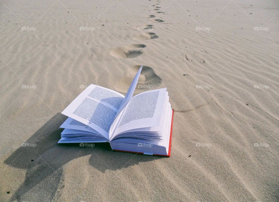 an open book lies on an empty sandy beach