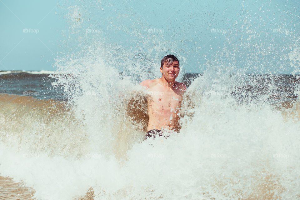 Young man enjoying the high waves in the sea during a summer vacations. Spending a summer holiday by the sea