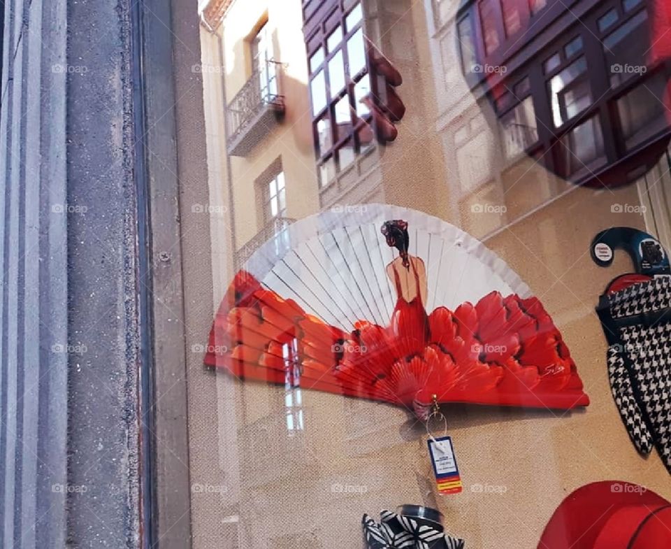 Fan with flamenco dancer in a souvenir shop window. The adjacent balconies are reflected in the windowpane. 
Red color scheme.