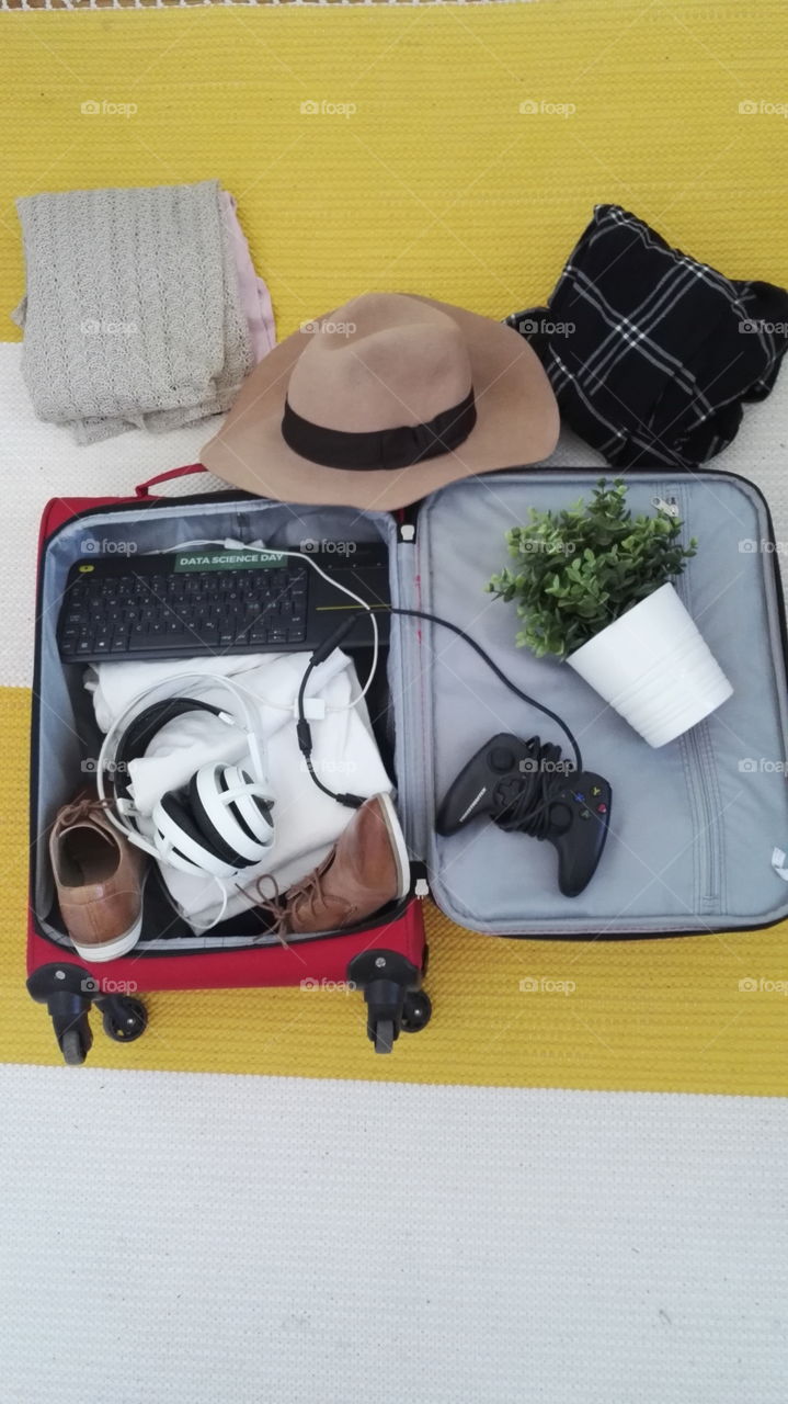 Chaotic packing for a vacation. Brown hat plant gaming headphones keyboard shoes and clothes.