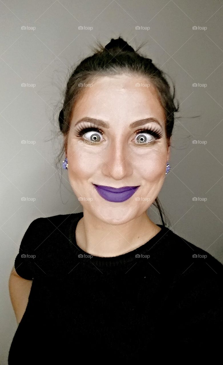 self portrait of a woman making a funny face wearing a purple lipstick smiling at the camera