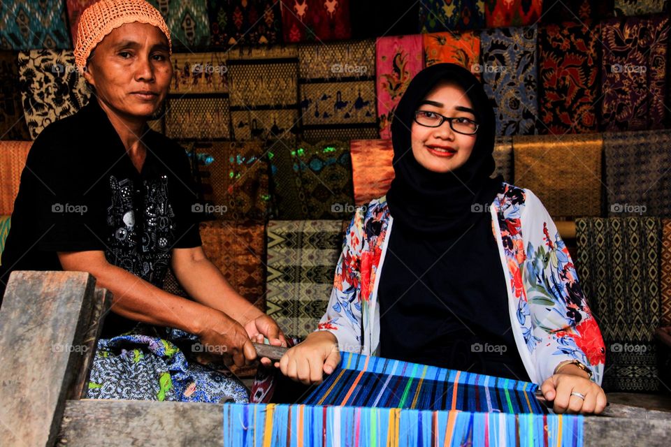 Portrait of a young woman sitting learning to weave cloth with traditional tools at a traditional cloth craft workshop in Sade village, with a happy expression, Lombok, Indonesia.