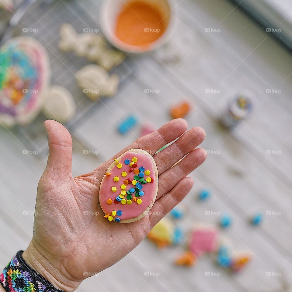 Woman’s hand holding egg shaped sugar cookie, closeup of a sugar cookie, bright pink egg cookie decoration with sprinkles, making cookies with toddlers, sugar cookies with toddlers, Easter time family traditions, making sugar cookies for the holidays