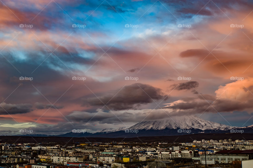 The evening city of Petropavlovsk-Kamchatsky in the background is a volcano, and above them are beautiful clouds painted with sunset colors