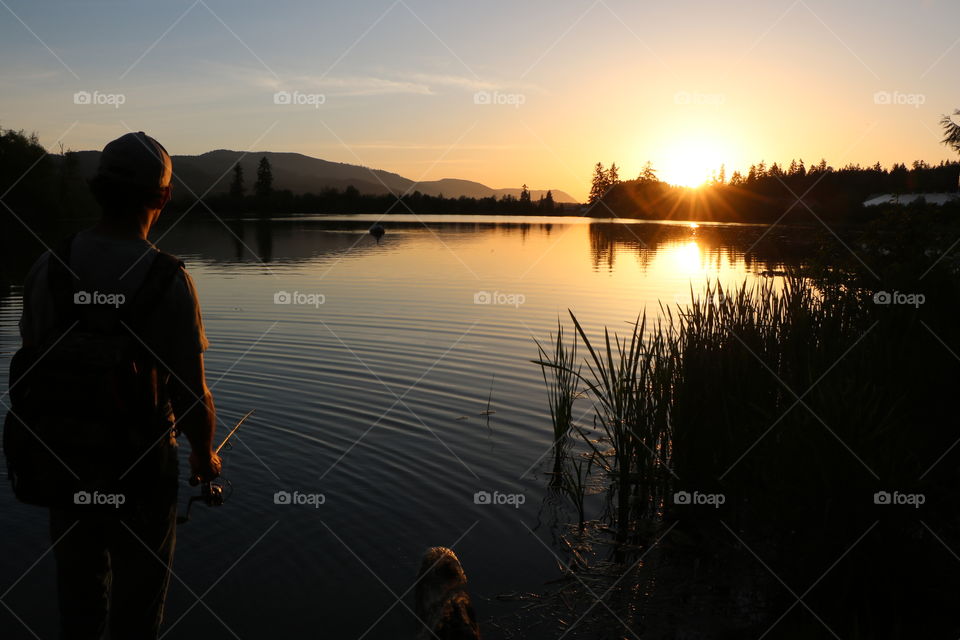 Young man fishing in the lake , while sun setting in and its golden light illuminating the crystal clear water