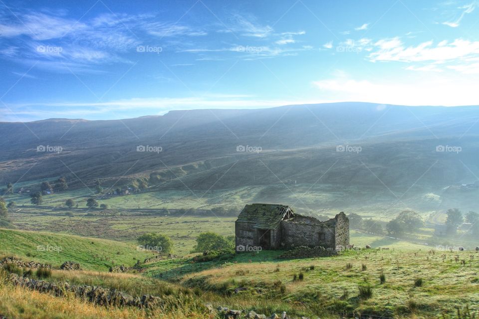 Derelict Farm Building. A disused barn sits on the side of a steep valley on a misty, sunny morning.