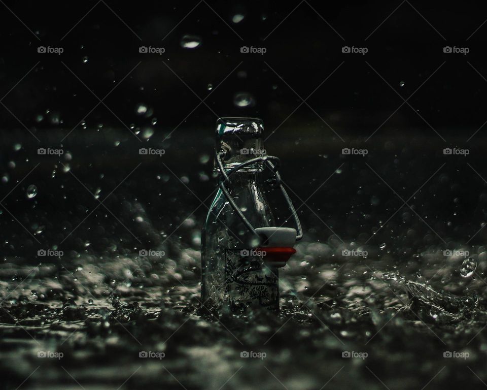 Glass bottle collects rain as water splashes around it