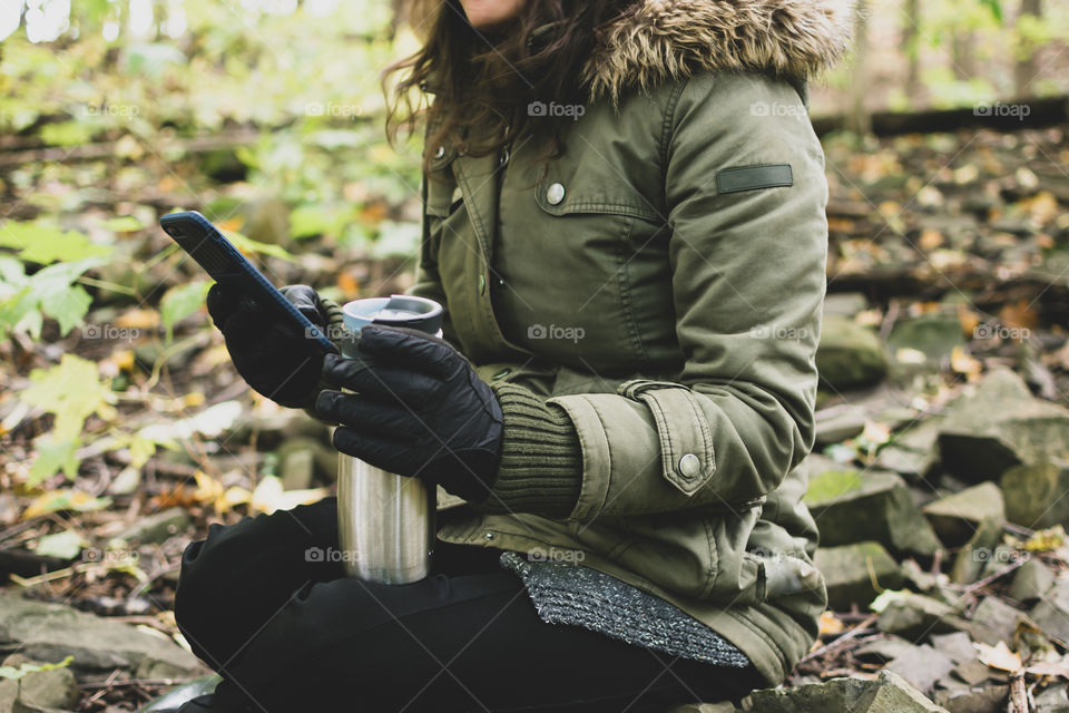 In the autumn forest taking a break with Isotoner sport Smartouch gloves using cell phone and drinking coffee cozy outdoor healthy lifestyle 