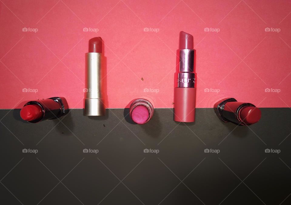 Five different colour lipsticks against a black and pink background captured from above.