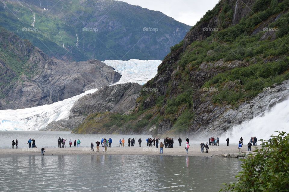 Tourists gather at the bottom of the massive Nugget Falls as Mendenhall Glacier appears in the background
