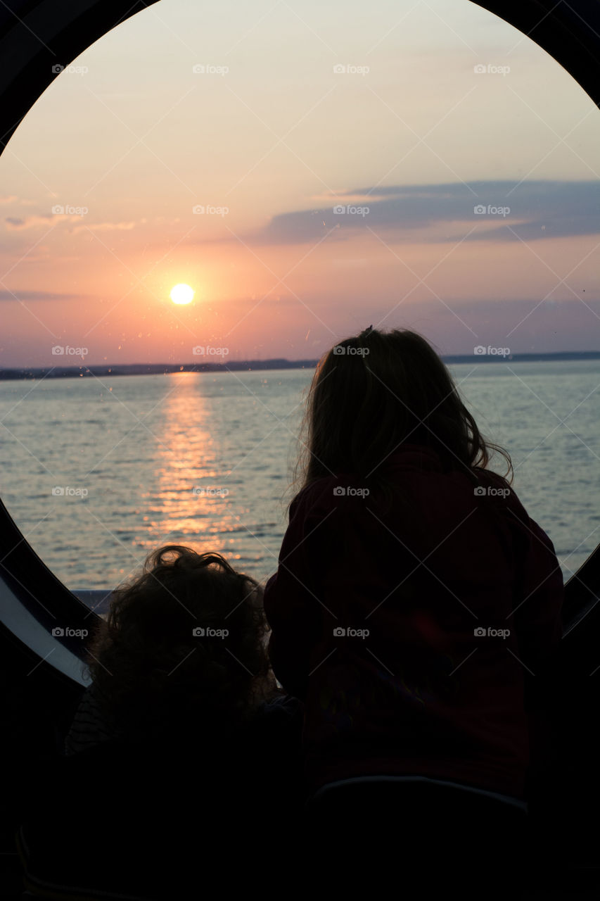 kids watching the sunrise. kids on circle shaped window on ferry boat watchin sun rising over the sea