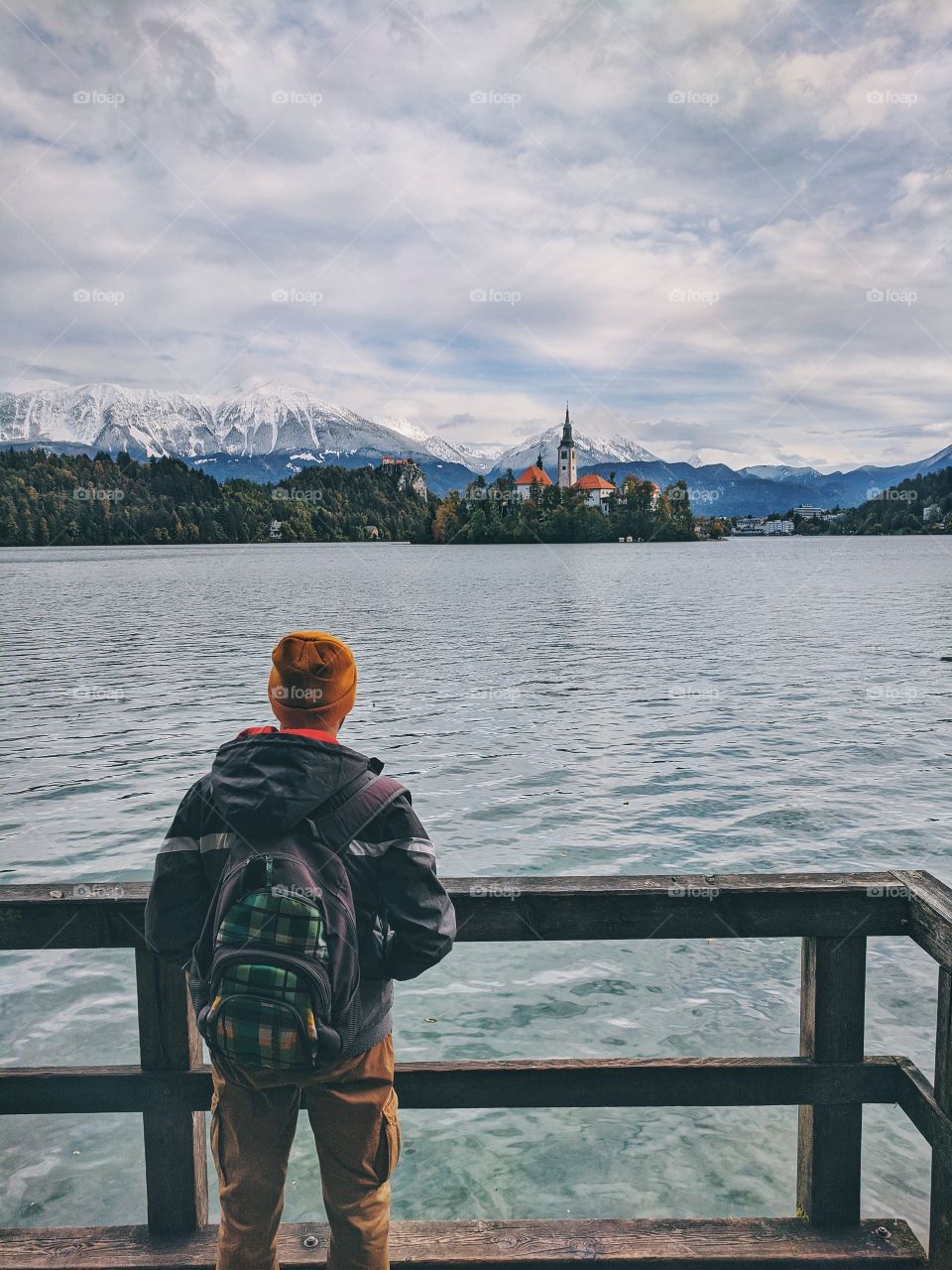 A male traveler stands on the road and admires the view of the snow-capped mountain peaks.