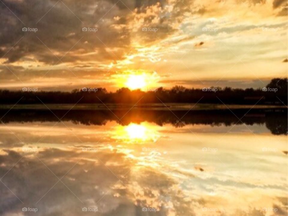 Reflection of silhouette trees and dramatic sky on lake