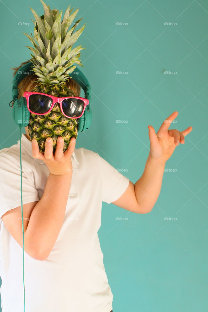 Teen holding a pineapple wearing sunglasses and headphones 