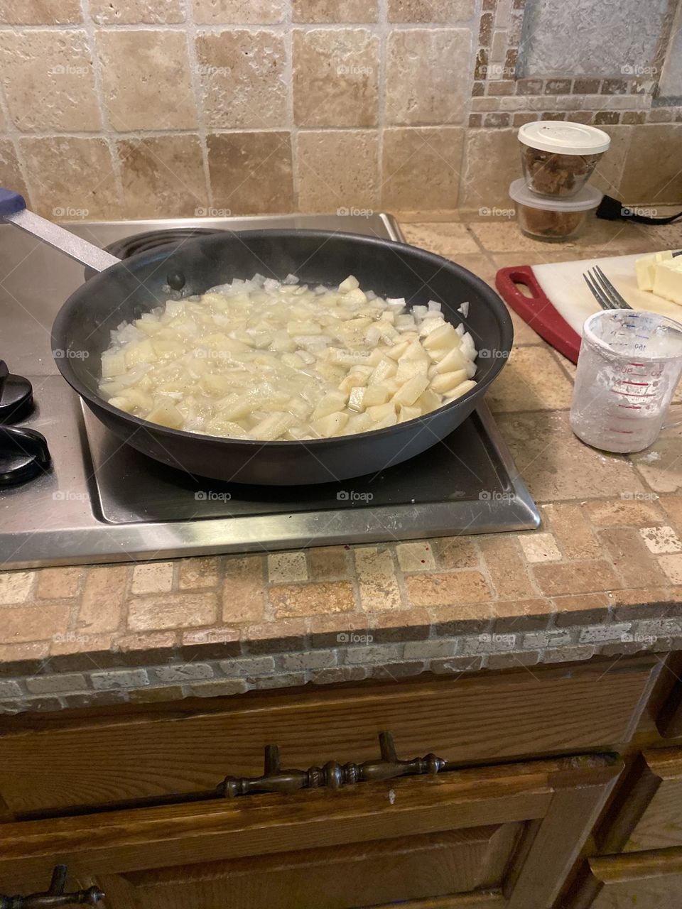 Sautéed onions in a pan on the stove in the kitchen with a measuring cup and cutting board next to it. 