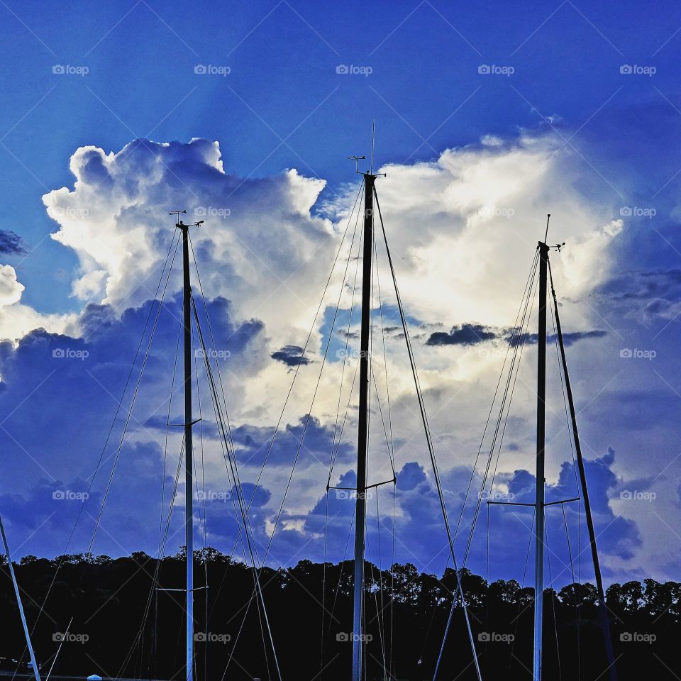 three sailboat masts against sunlit clouds
