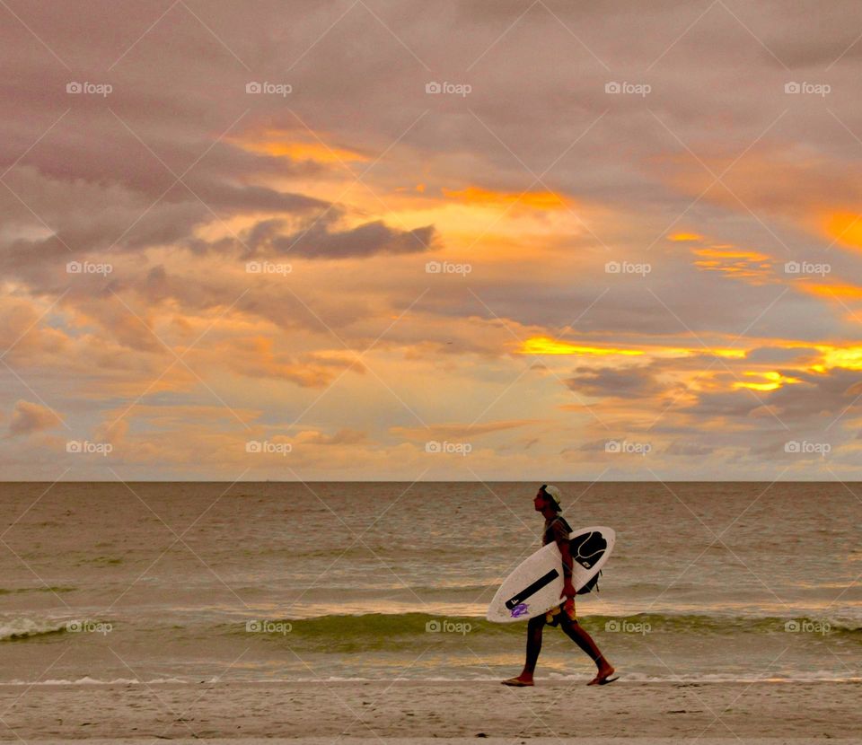 Surfer carrying his board along the beach at sunset