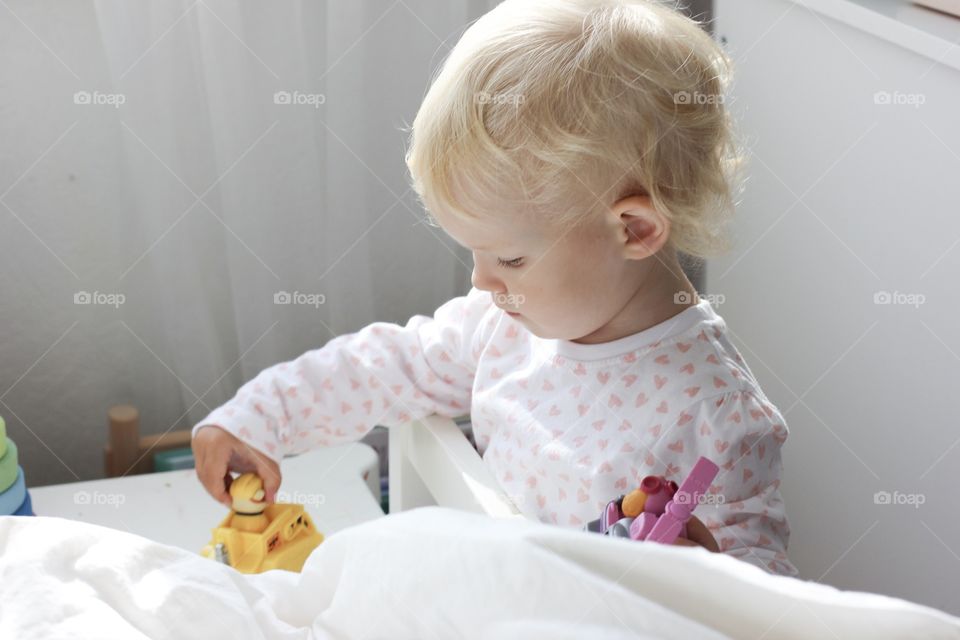 Blonde baby girl playing with toys on table in the lights of a sun