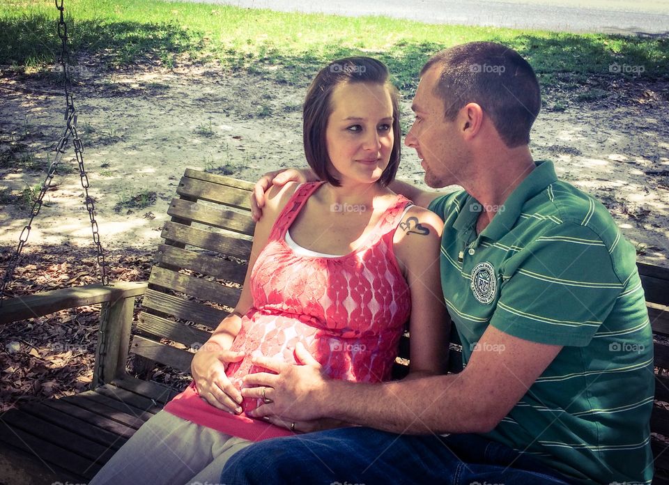 Husband with his pregnant wife sitting on wooden swing